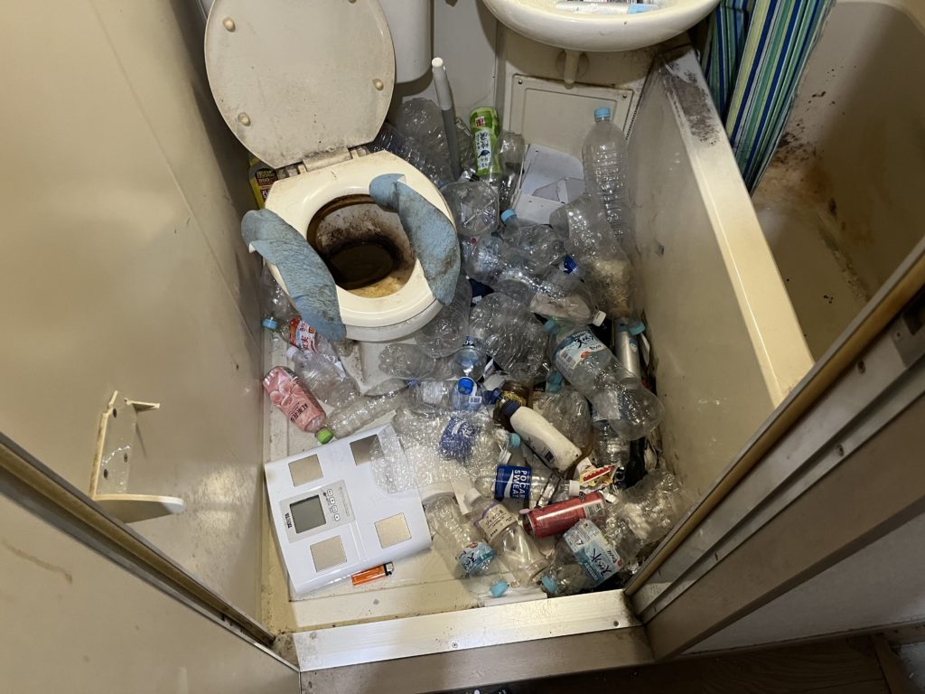 詰まって使えないトイレと床に転がるペットボトル